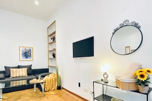 Un salon moderne avec un canapé, une table basse, un téléviseur et un grand miroir rond accroché au mur.