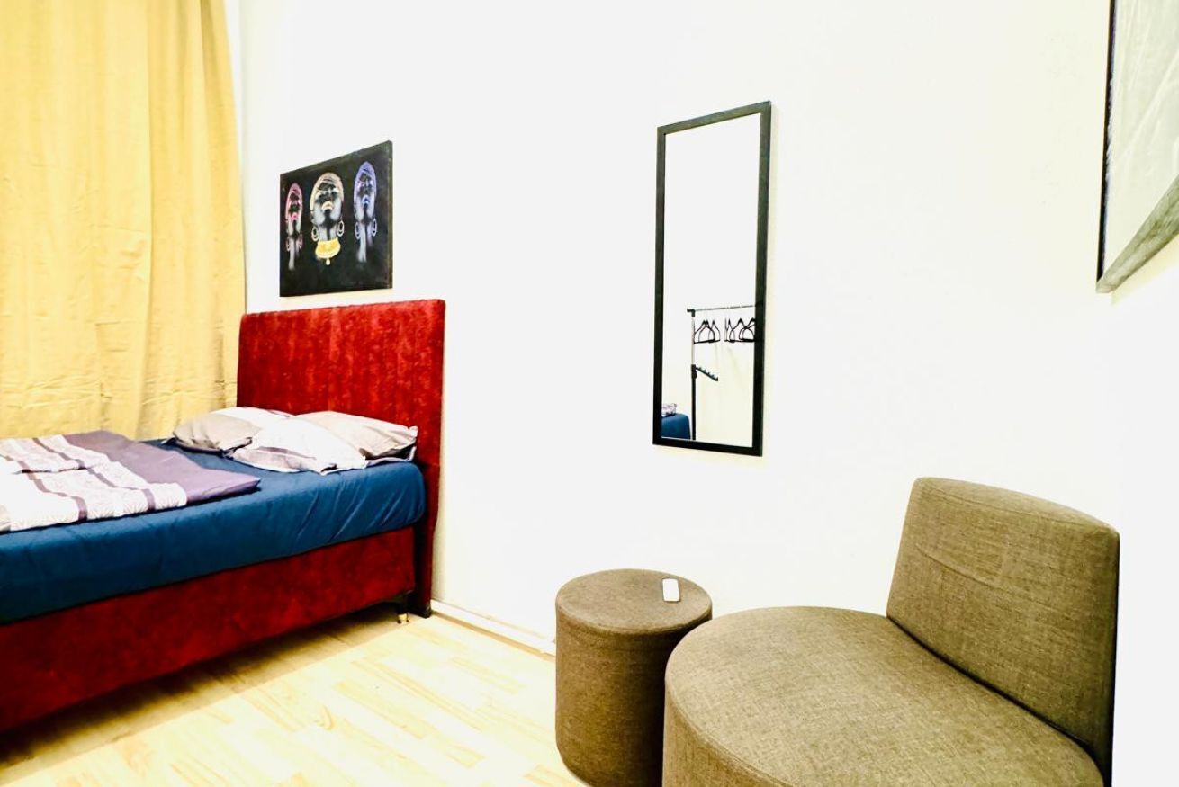 Une pièce comprenant un lit, un tabouret rond, un canapé, un miroir encadré et un tableau accroché au mur.