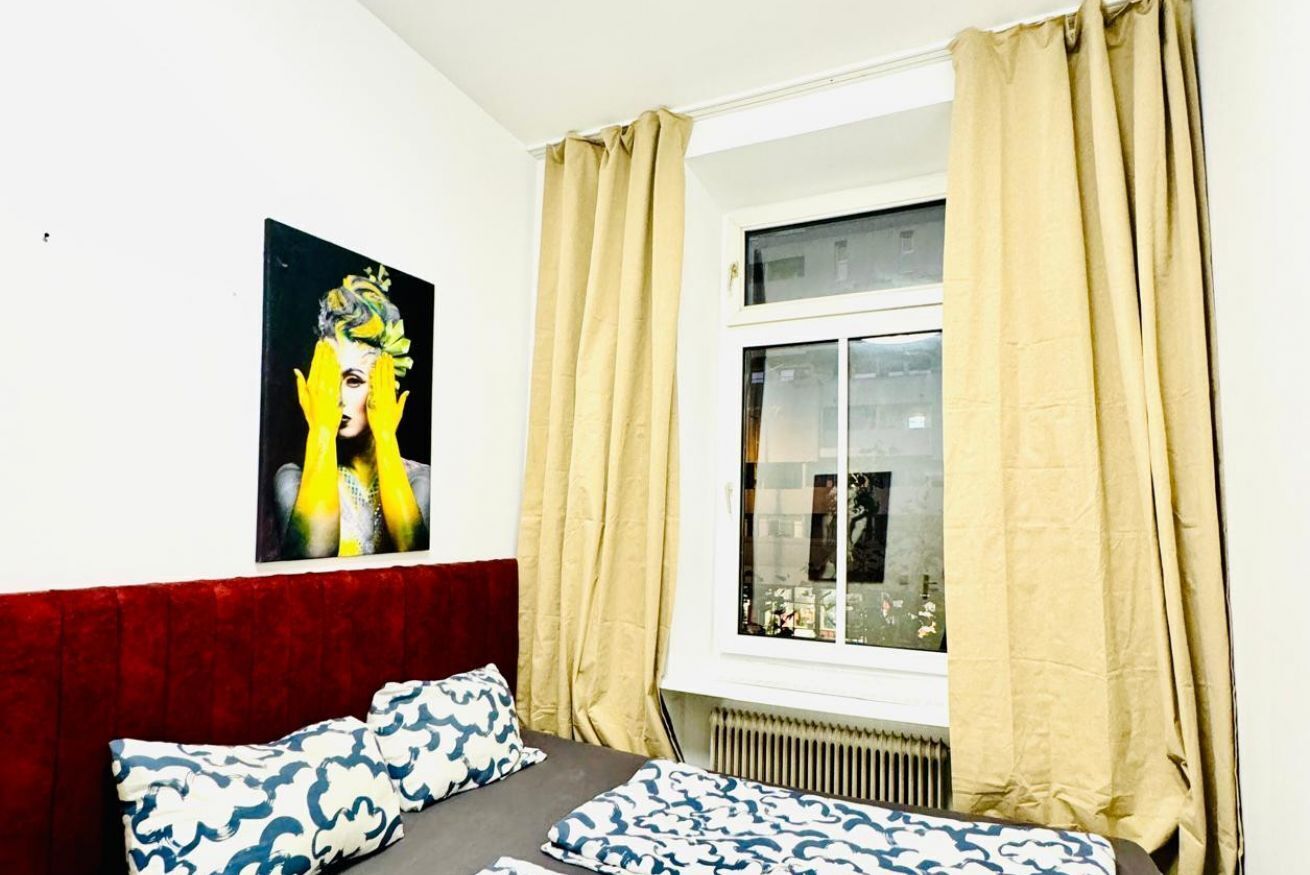 A bedroom with a bed, a window with curtains, a radiator, and a wall-mounted painting.