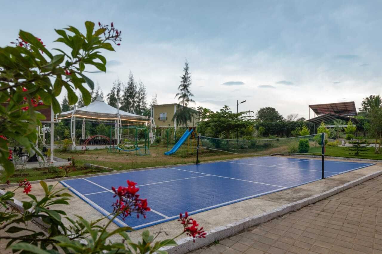 A blue outdoor tennis court with a net, surrounded by greenery and a gazebo.