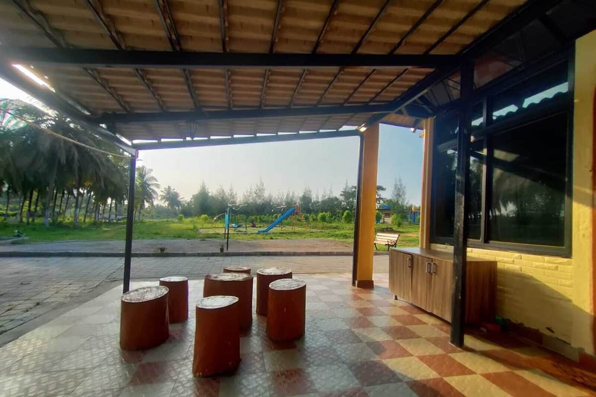 Ein überdachter Außenbereich mit Fliesenboden, einer Bank und Blick auf einen Spielplatz in der Ferne.
