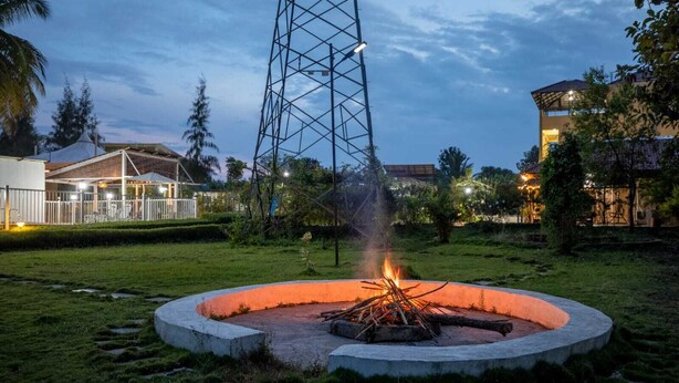 A circular fire pit with a metal structure in the center, surrounded by grass and trees. - Encanto Farmstay Resort (Hunsur)