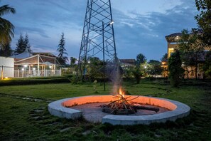 Un hoyo para fuego circular con una estructura metálica en el centro, rodeado de césped y árboles.