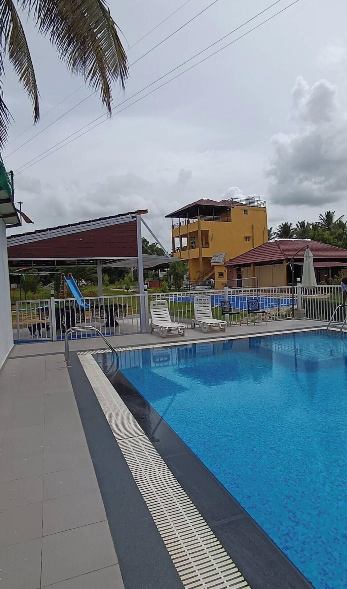 A swimming pool with a tiled deck, a covered children's play area, and a yellow building in the background.