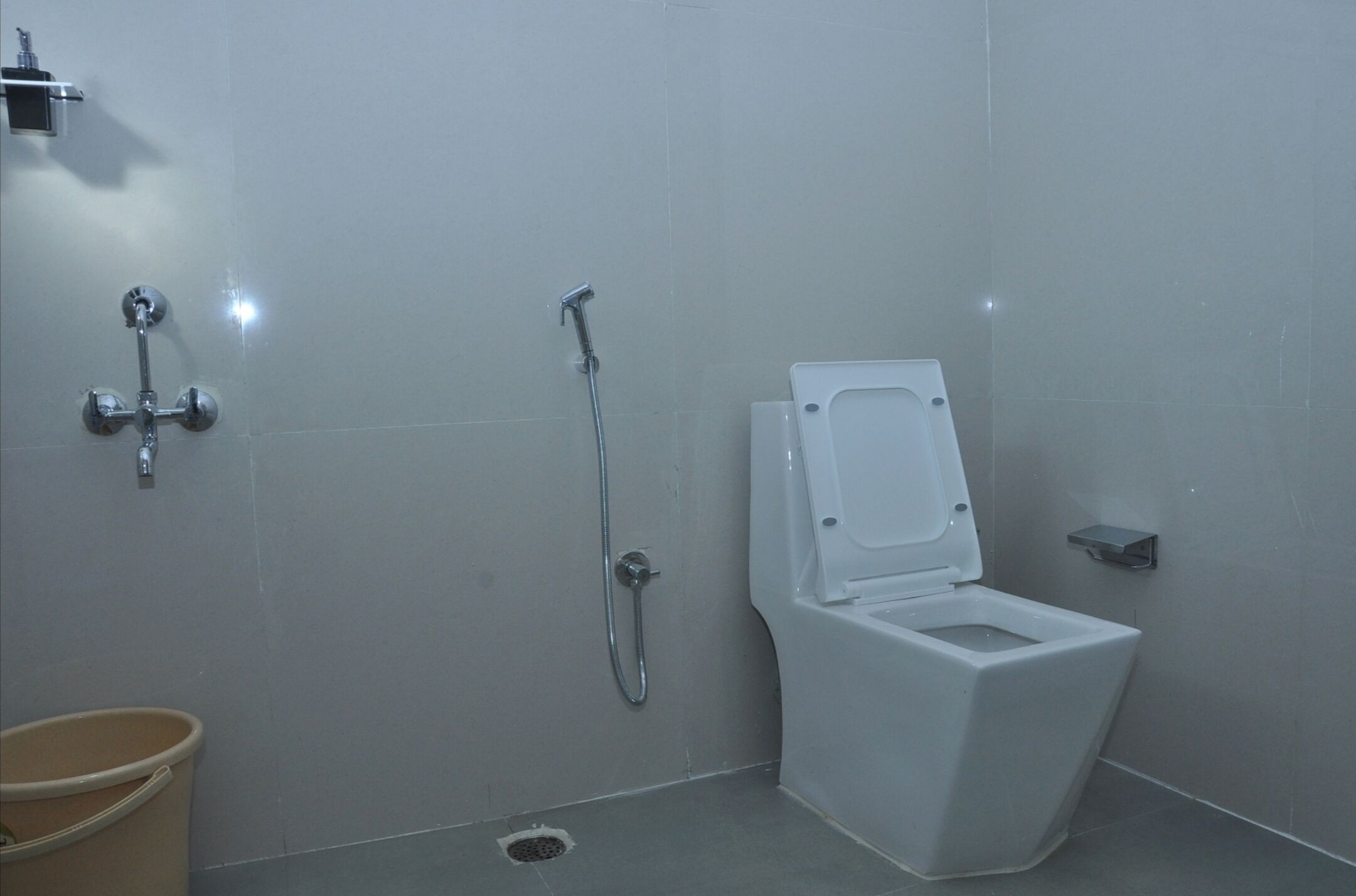 Un baño pequeño y moderno con inodoro blanco, cabezal de ducha y un estante.