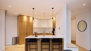 Een moderne keuken met houten kastjes, een witte aanrecht en drie zwarte barkrukken.