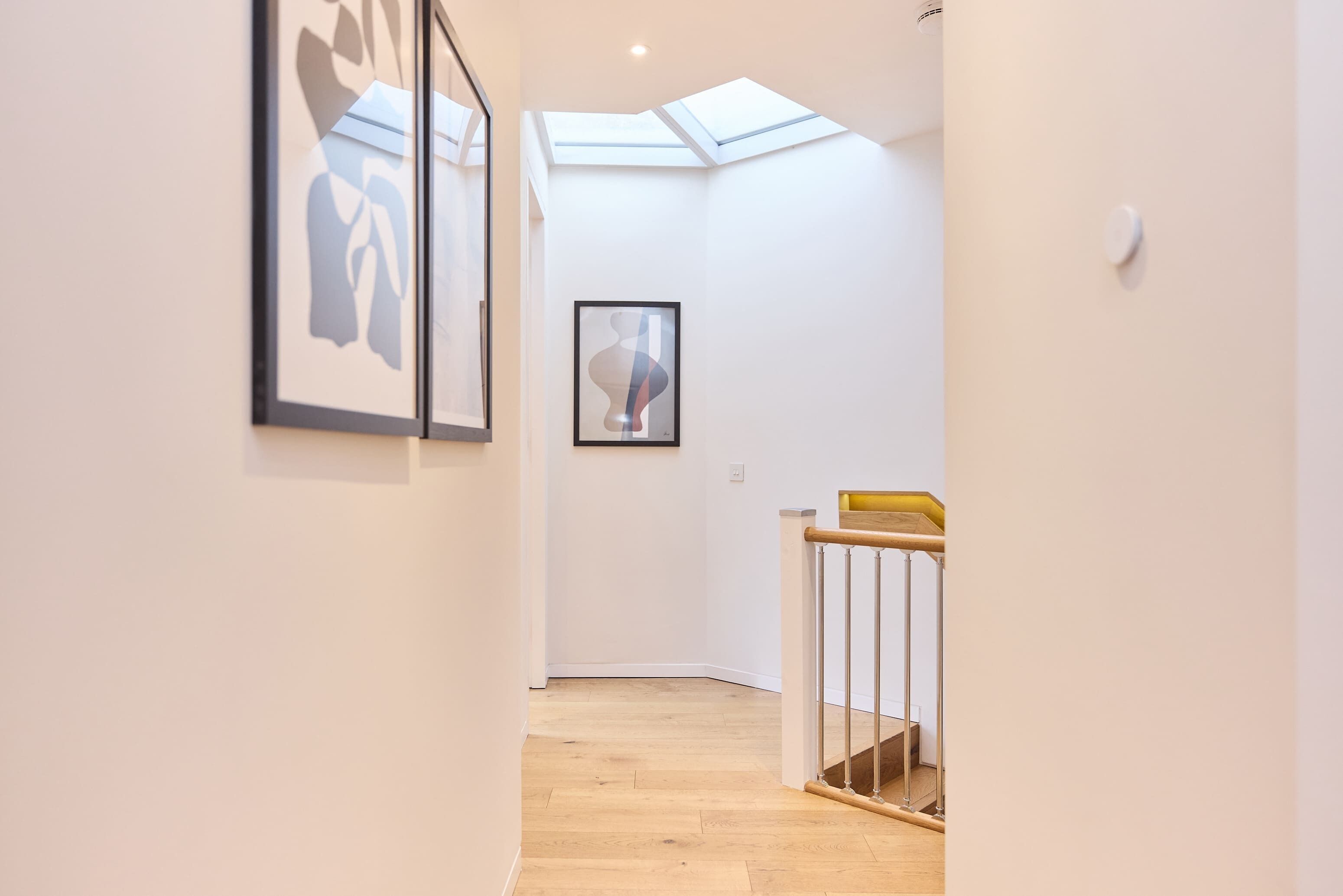 A hallway with a skylight, framed artwork on the walls, and a wooden staircase.