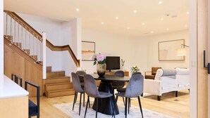 Een moderne woonkamer met een eethoek, een houten trap en een flatscreen televisie.