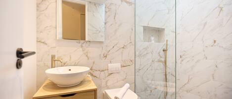 A modern bathroom with a marble sink, a toilet, and a glass-enclosed shower.