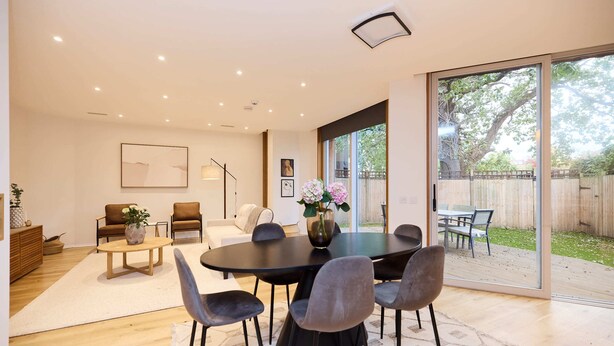 Een moderne woonkamer met een ronde tafel, zes stoelen, een bank en een grote glazen schuindeur die leidt naar een achtertuin.