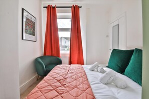 A hotel room with a bed, a chair, a window with curtains, and a framed picture on the wall. - Cosy 3-bedroom House Near Caerphilly Castle (Caerphilly)