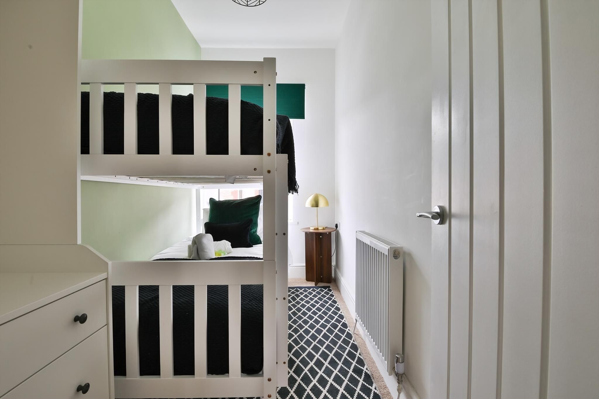 A bunk bed room with a radiator, a lamp, and a door.