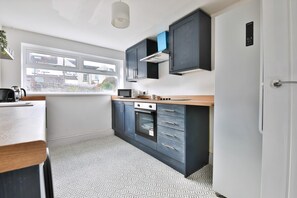Une cuisine moderne dotée d’une fenêtre, d’un four encastré, d’un four à micro-ondes et de meubles de rangement aux couleurs sombres.