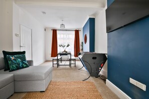 A modern living room with a grey sofa, a small table, and a foosball table. - Cosy 3-bedroom House Near Caerphilly Castle (Caerphilly)