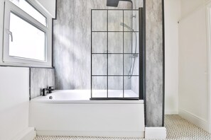 Une salle de bain moderne avec une baignoire, un espace douche et une fenêtre.