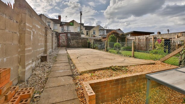 Una zona residencial con un camino pavimentado, un muro de ladrillo y un jardín cercado.