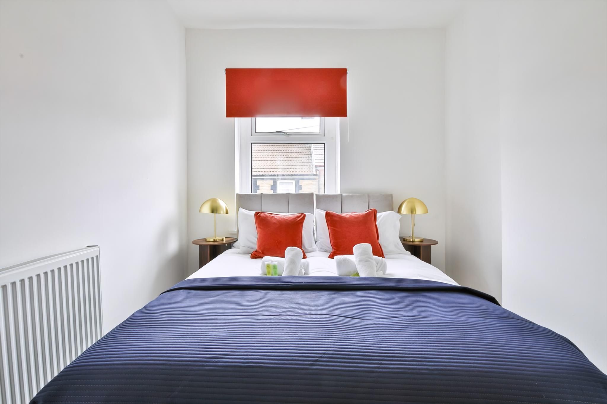 Ein Hotelzimmer mit Bett, Fenster, Heizkörper und zwei Nachttischlampen.