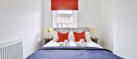 A hotel room with a bed, a window, a radiator, and two bedside lamps.