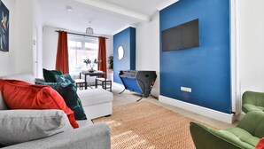 Una sala de estar con un sofá, un sillón verde, una cinta de correr y un televisor montado en una pared azul.