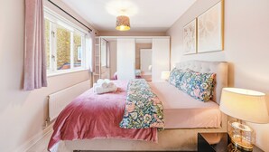 Une chambre à coucher avec un lit, une table de chevet avec une lampe, une fenêtre avec des rideaux et un radiateur.