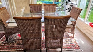 Zona pranzo con sedie in vimini e tavolo in vetro, con vista su un giardino e una cascata.