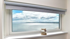 A window with a view of a body of water and a cloudy sky. - Impressive Beach View Duplex Penthouse (Swansea)