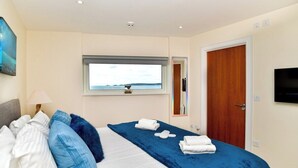 A hotel room with a bed, a window with a view, a door, and a TV on the wall. - Impressive Beach View Duplex Penthouse (Swansea)