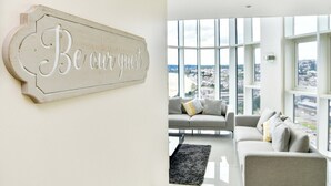 A modern living room with a large window, a sofa, and a sign that reads "Be our guest". - Impressive Beach View Duplex Penthouse (Swansea)