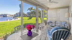 A room with a large window overlooking a marina and a grassy area. There is a table with a purple vase and a blue chair.