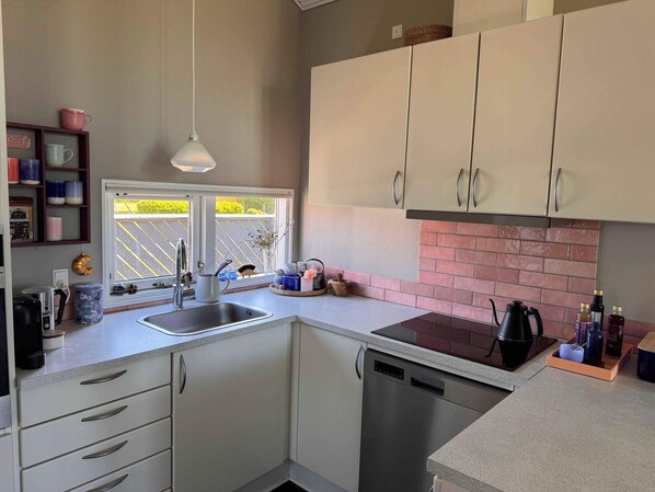 A modern kitchen with white cabinets, a stainless steel dishwasher, and a window with a view of a garden. - 4 Star Holiday Home in Skaelskor (Skælskør)