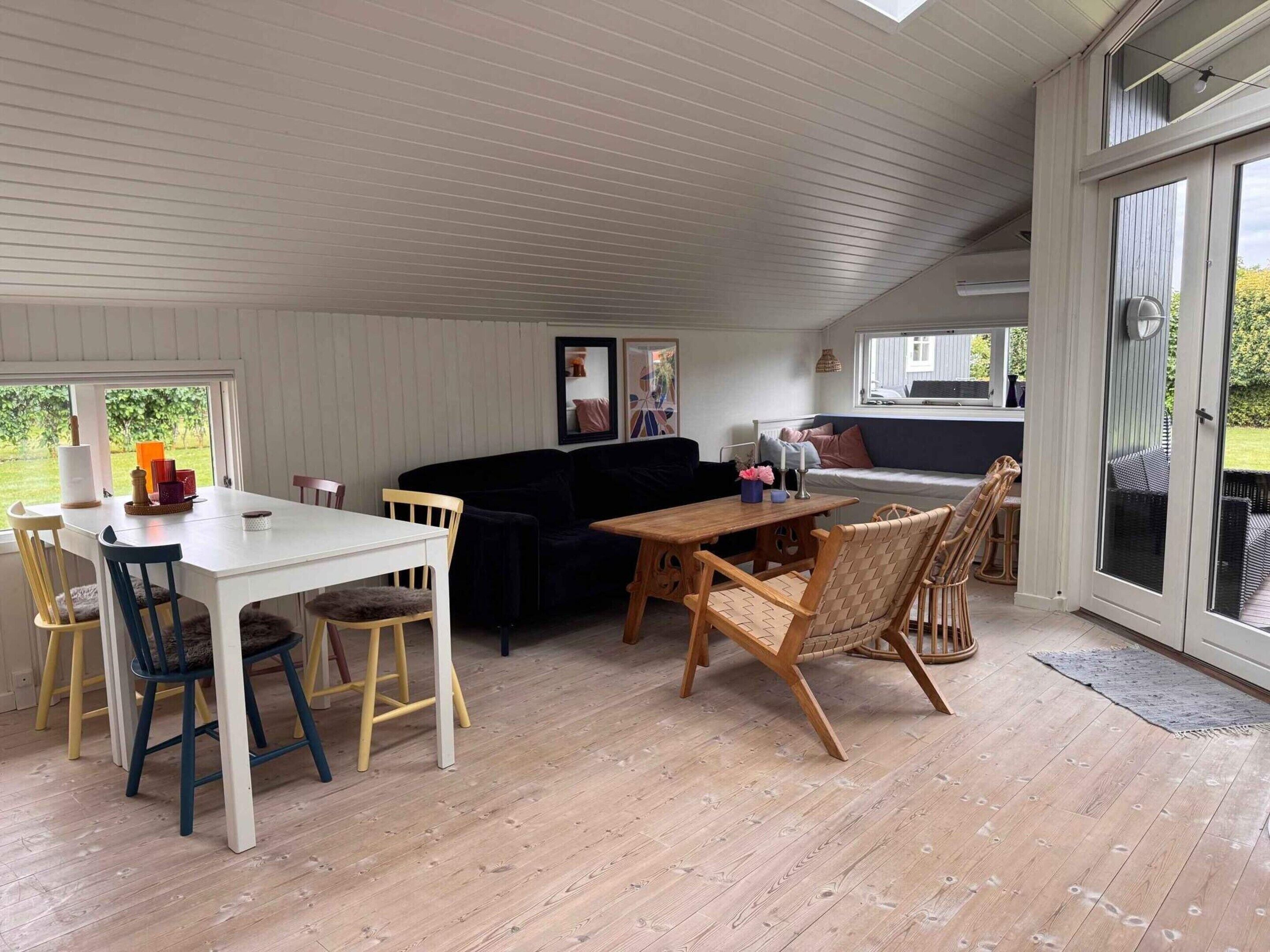 A cozy indoor space with a dining table, chairs, a sofa, and a large window.