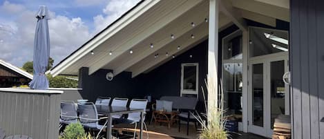 A covered outdoor patio with a dining area, potted plants, and a wooden deck.