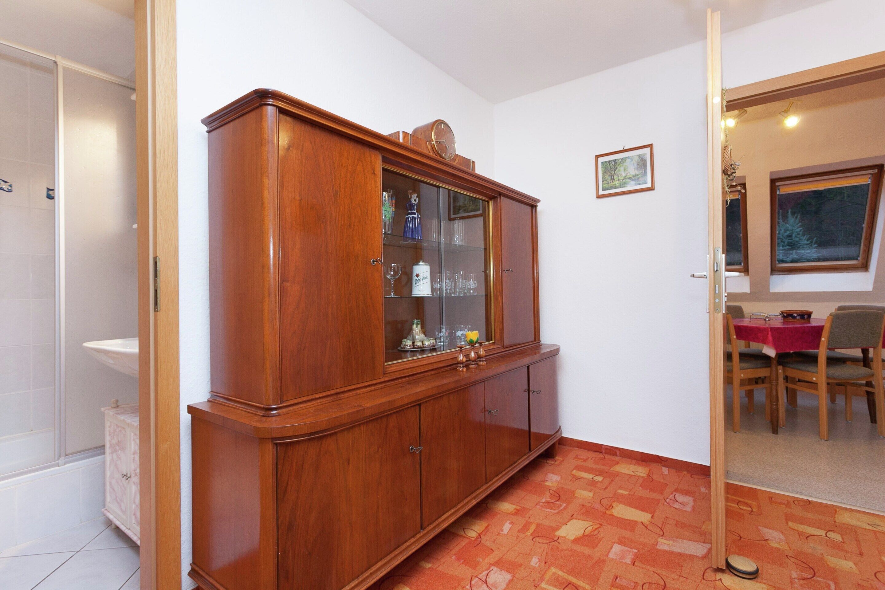 A room with a wooden cabinet, a dining table with chairs, and a window.