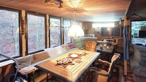 A cozy cabin interior with a dining table, chairs, a sofa, and large windows offering a view of the forest. - Gemutliche Wohnung mit Kamin in Dresden-freital (Freital)