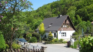 A house with a sloped roof, surrounded by lush greenery and trees. - Gemutliche Wohnung mit Kamin in Dresden-freital (Freital)