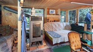 A cozy cabin interior with a bed, a fireplace, a wooden ceiling, and a window with a view of trees. - Gemutliche Wohnung mit Kamin in Dresden-freital (Freital)