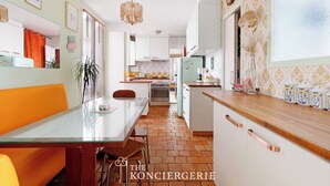 A kitchen with a central island, a dining area with a glass table, and a kitchen counter with decorative items. - Elegance & confort - Paris Bouvines 5P (Paris)