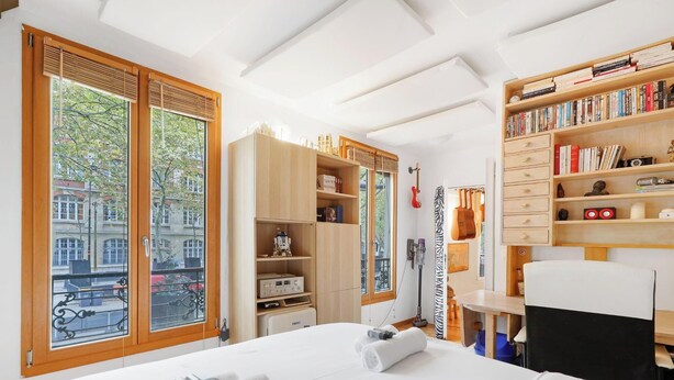 A hotel room with a large bed, wooden wardrobe, bookshelf, and a view of the city through large windows. - Elegance & confort - Paris Bouvines 5P (Paris)