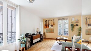 A cozy living room with a wooden floor, a piano, a bookshelf, and a dining area with a table and chairs. - Elegance & confort - Paris Bouvines 5P (Paris)