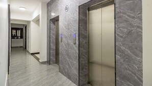 A hallway with two elevators, marble walls, and a security camera. - Chic One Bedroom with Swimming Pool, Gym and magnificent City Views (Nairobi)