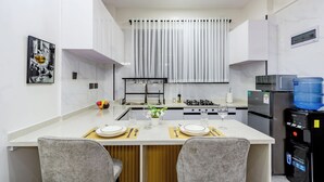 A modern kitchen with a central island, a dining area, and a refrigerator. - Chic One Bedroom with Swimming Pool, Gym and magnificent City Views (Nairobi)