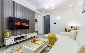A modern living room with a flat-screen TV displaying 'NETFLIX', a white sofa, a coffee table with decorative items, and a striped wall.