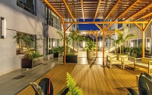 A covered outdoor area with wooden flooring, potted plants, and seating arrangements. - Chic One Bedroom with Swimming Pool, Gym and magnificent City Views (Nairobi)