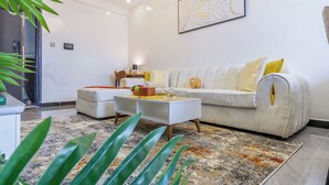 A modern living room with a white sofa, a coffee table, and a patterned rug. - Chic One Bedroom with Swimming Pool, Gym and magnificent City Views (Nairobi)