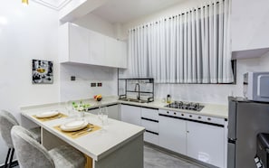 A modern kitchen with white cabinetry, a central island with seating, a gas stove, and a microwave. - Chic One Bedroom with Swimming Pool, Gym and magnificent City Views (Nairobi)