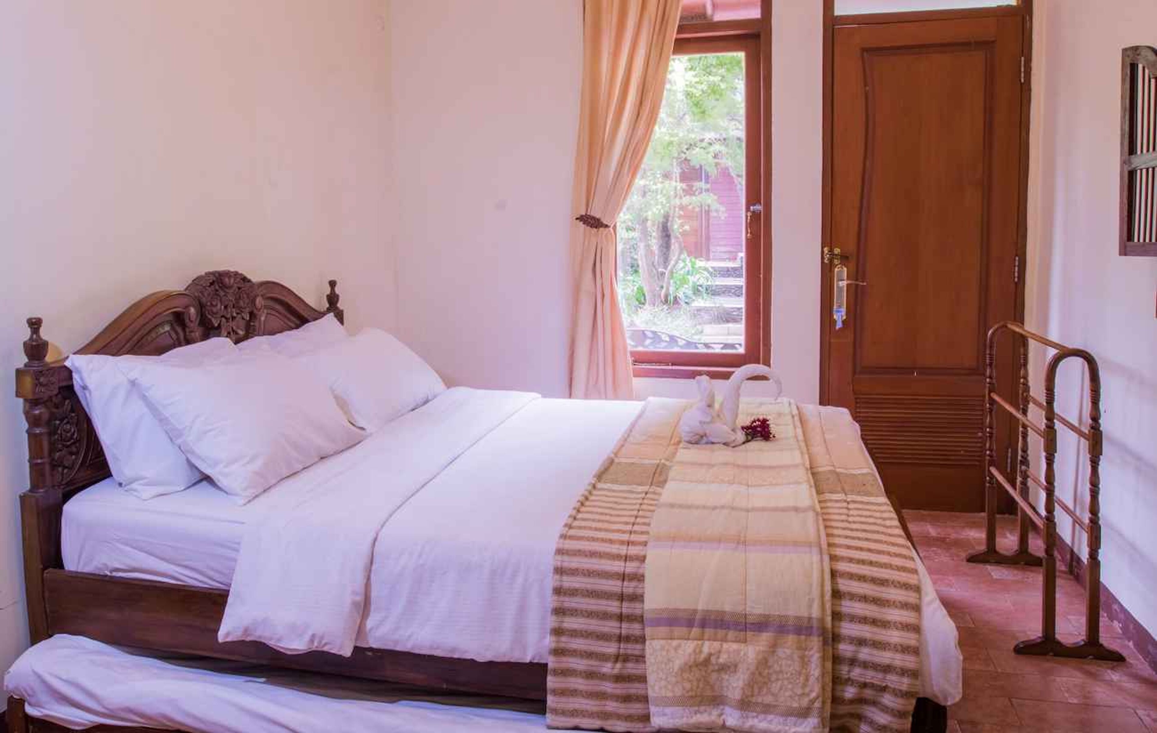 Una cama bien hecha con sábanas blancas y una manta a rayas, una puerta de madera y una ventana con cortinas.