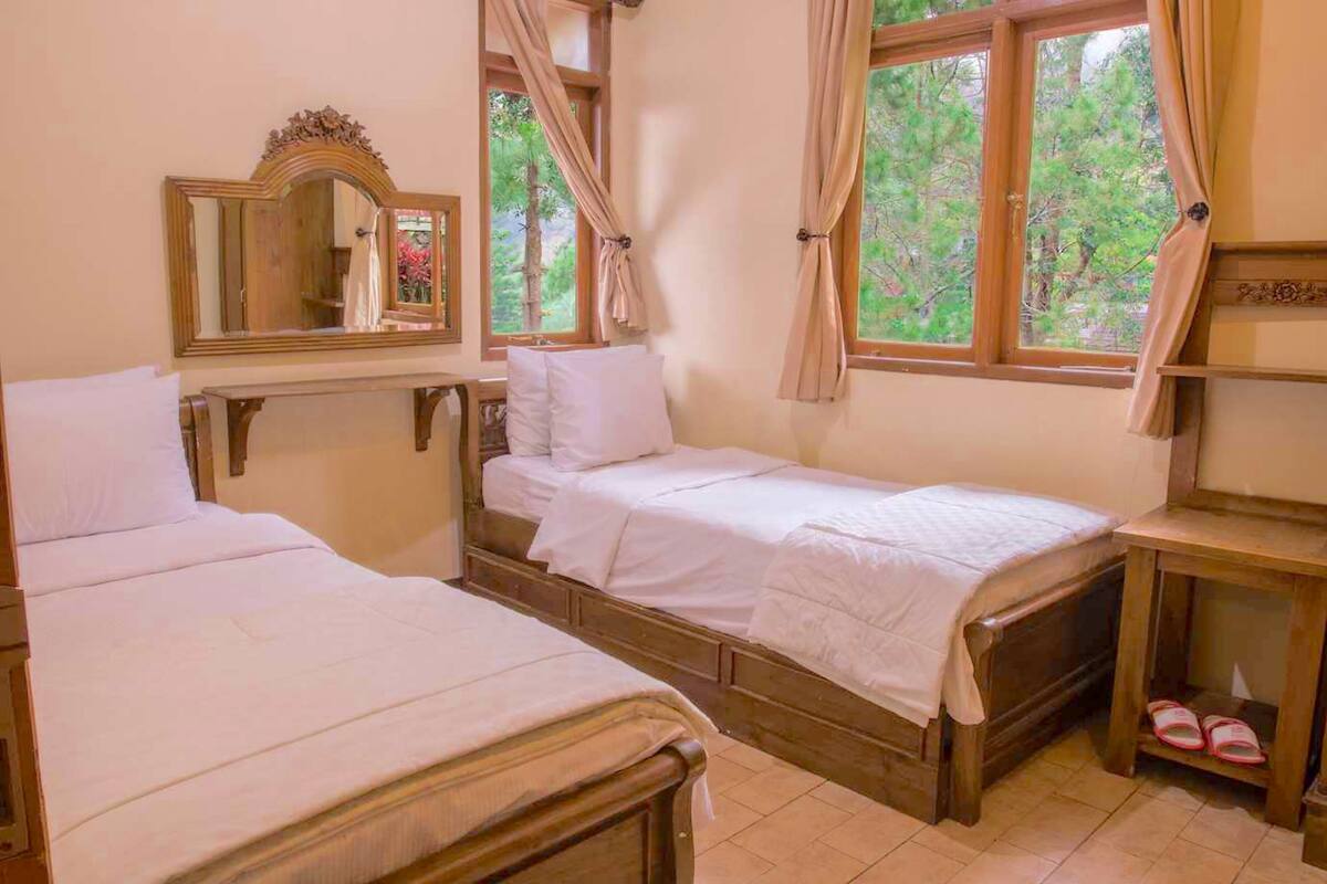 Quarto com duas camas de madeira, um espelho e uma janela com cortinas.
