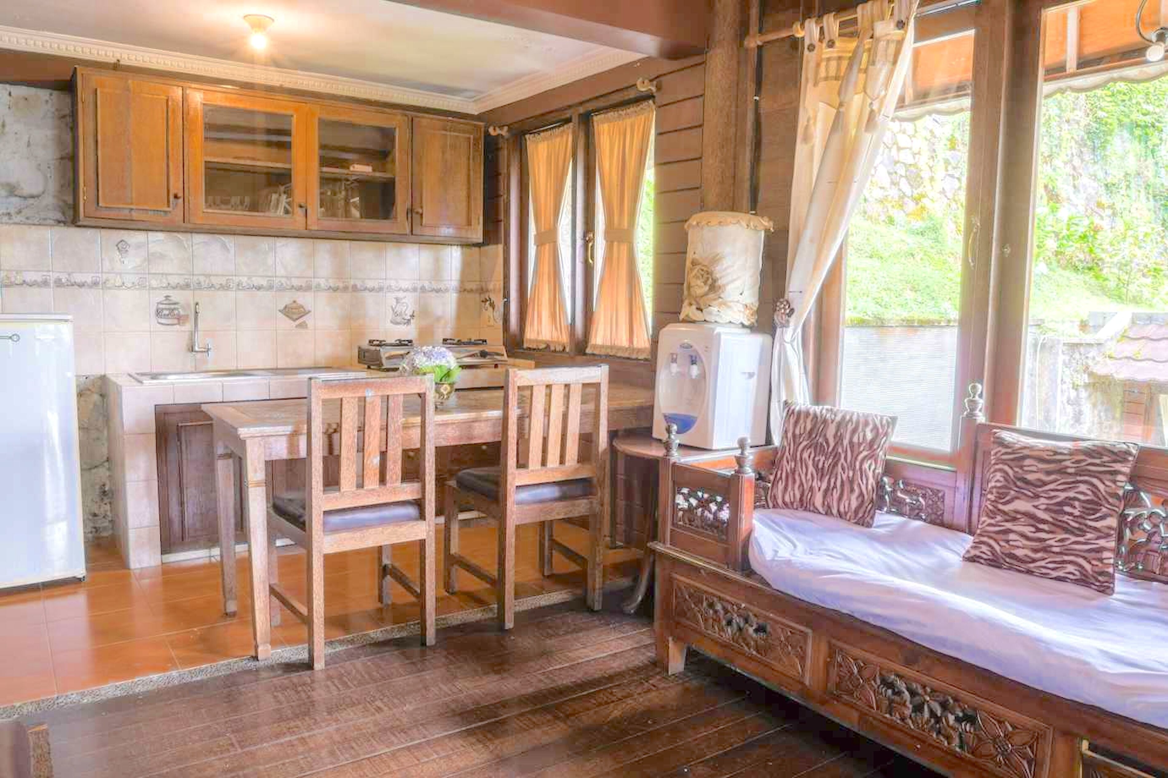 Um quarto acolhedor com uma cama de madeira, uma mesa pequena e cadeiras. Há uma janela com cortinas e vista para o verde lá fora.