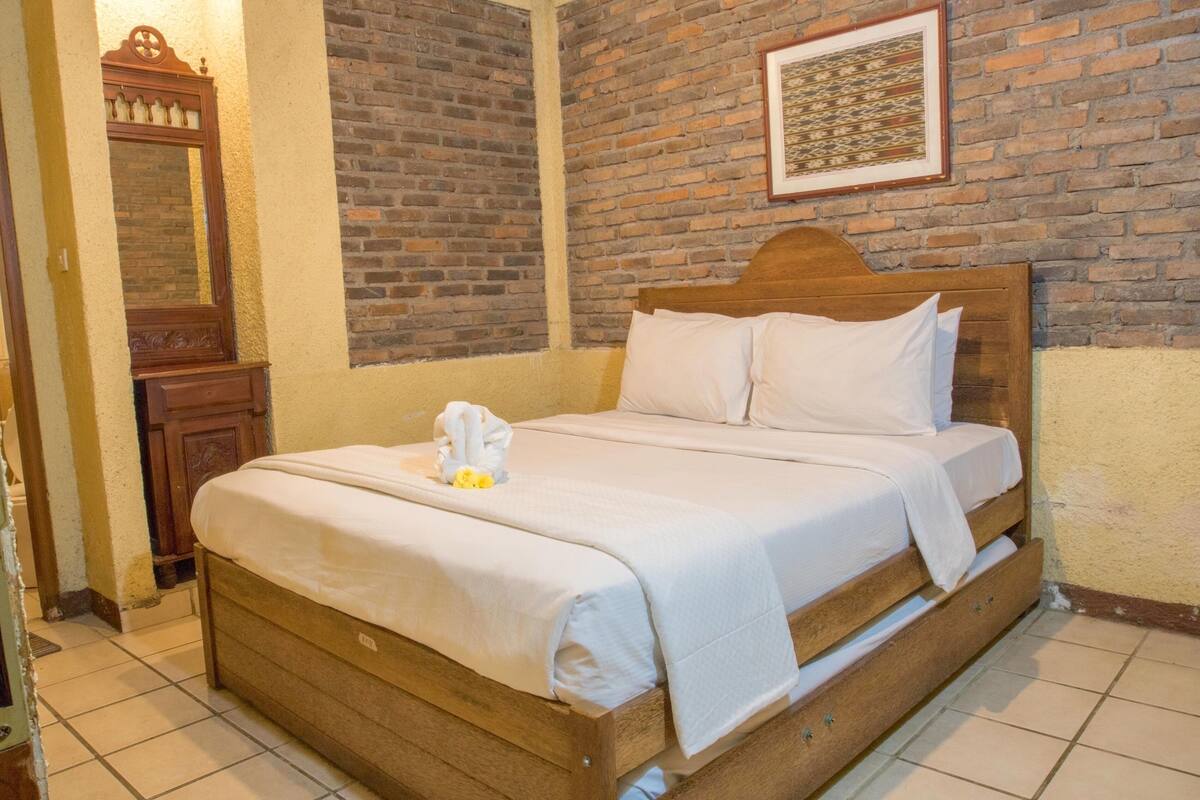 Uma cama de solteiro com cabeceira de madeira, roupa de cama branca e uma toalha com flores sobre a cama.