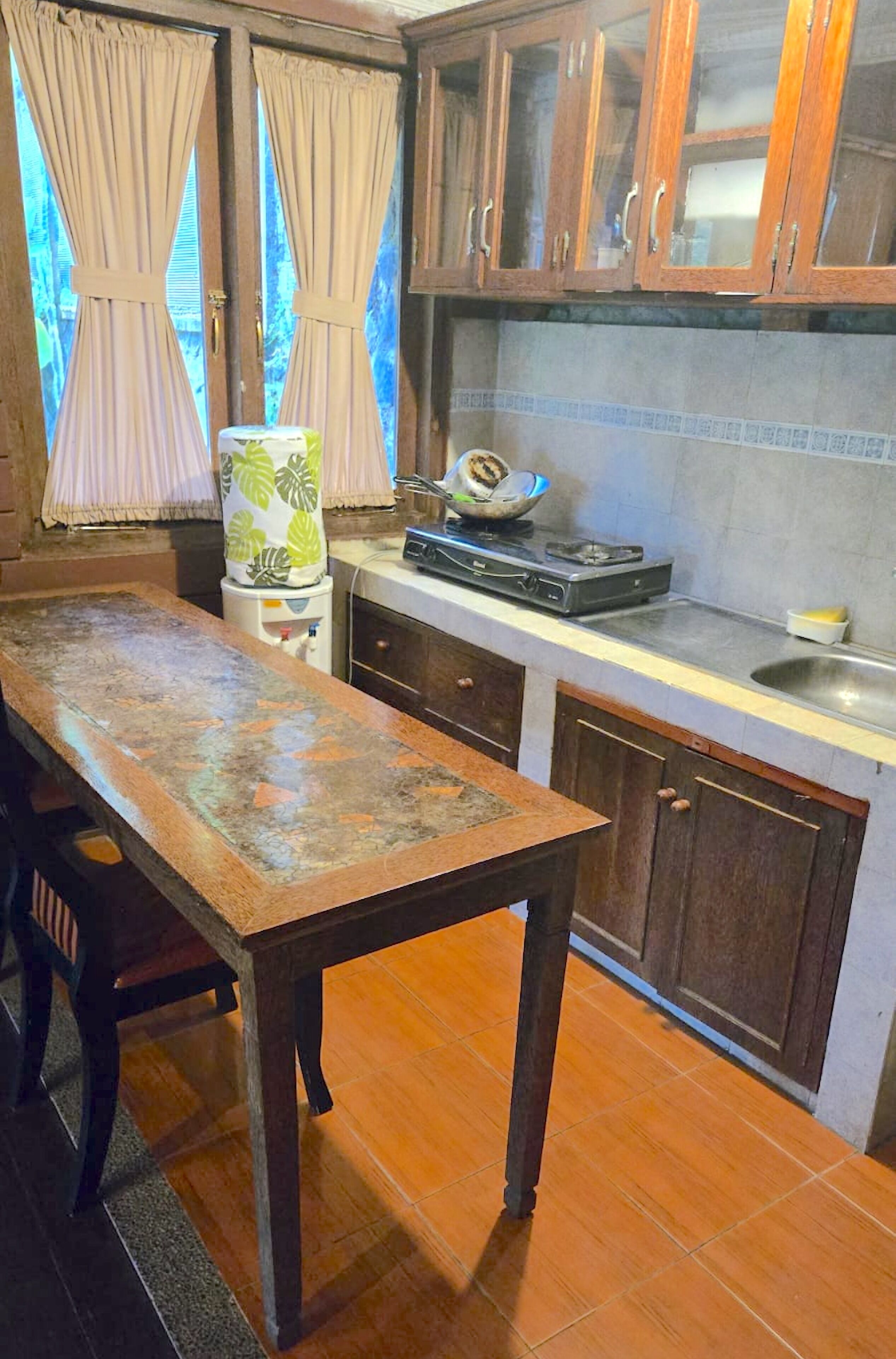 A kitchen with a wooden table, cabinets, and a window with curtains.